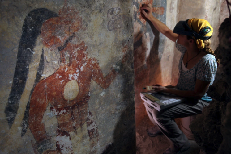 Angelyn Bass cleans and stabilizes the surface of a wall that shows the figure of a man who may have been the town scribe.Credit...Tyrone Turner/National Geographic.