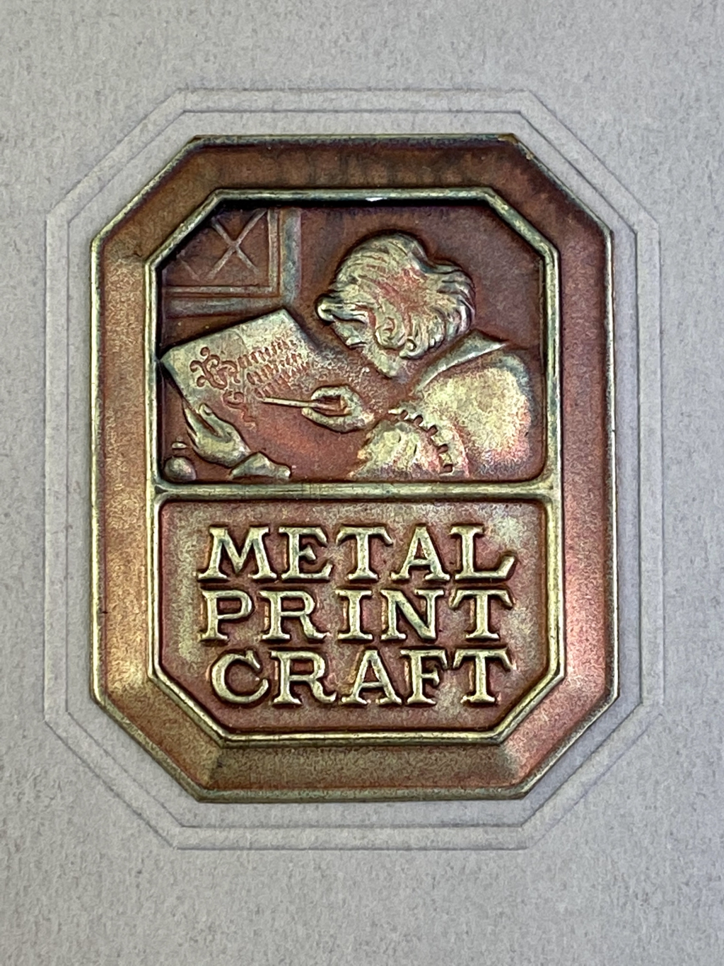 Enlargement to show detail of embossed metal emblem of a scribe writing a manuscript published by L. G. Grammes & Sons in 1926.