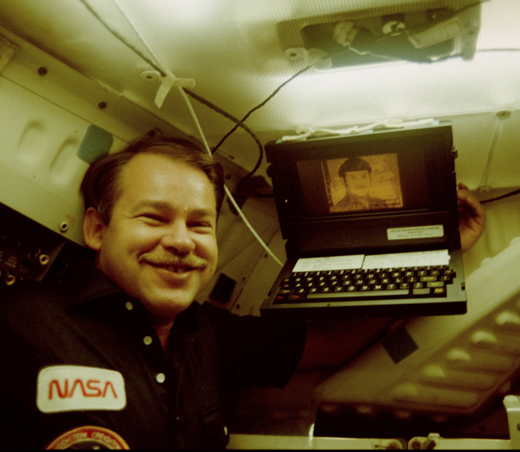 Astronaut John O. Creighton posing with onboard GRiD Compass computer, displaying a likeness of Mr. Spock of Star Trek