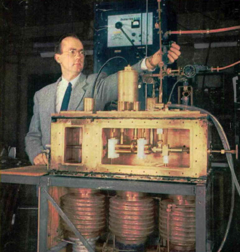 First prototype ammonia maser and inventor Charles H. Townes. The ammonia nozzle is at left in the box, the four brass rods at center is the quadrupole state selector, and the resonant cavity is at right. The 24 GHz microwaves exit through the vertical waveguide Townes is adjusting. At bottom are the vacuum pumps.