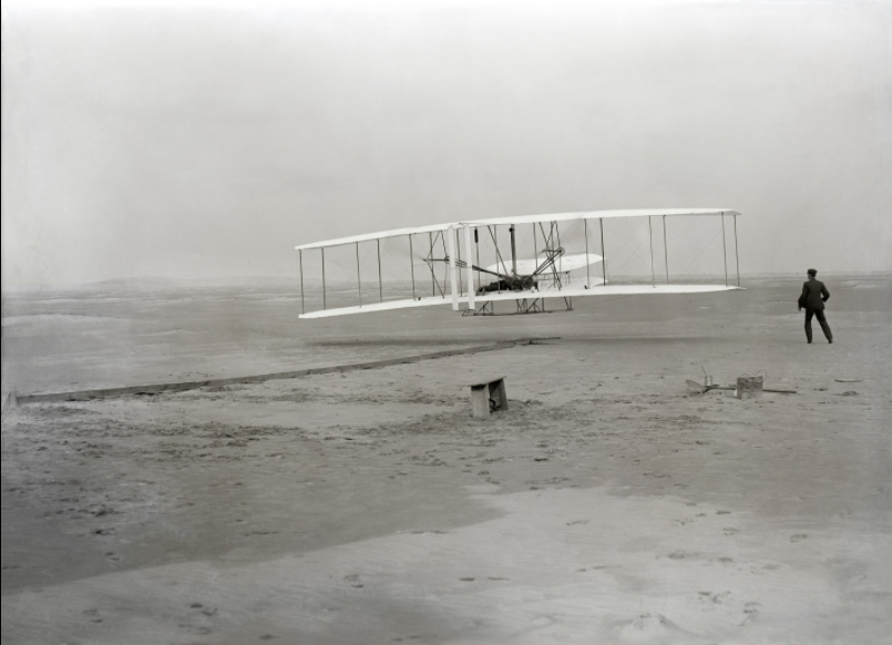 First flight of the Wright Flyer, December 17, 1903, Orville piloting, Wilbur running at wingtip.